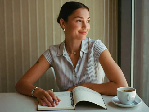 Ad creative — woman at a cafe with her notebook, relaxed